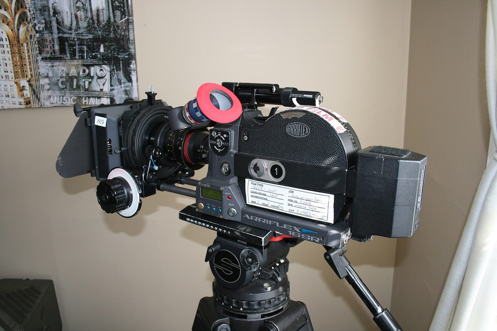A loaded Arriflex 16SR 16mm film camera on a fluid-head tripod with matte box, follow focus and a film label on the magazine.