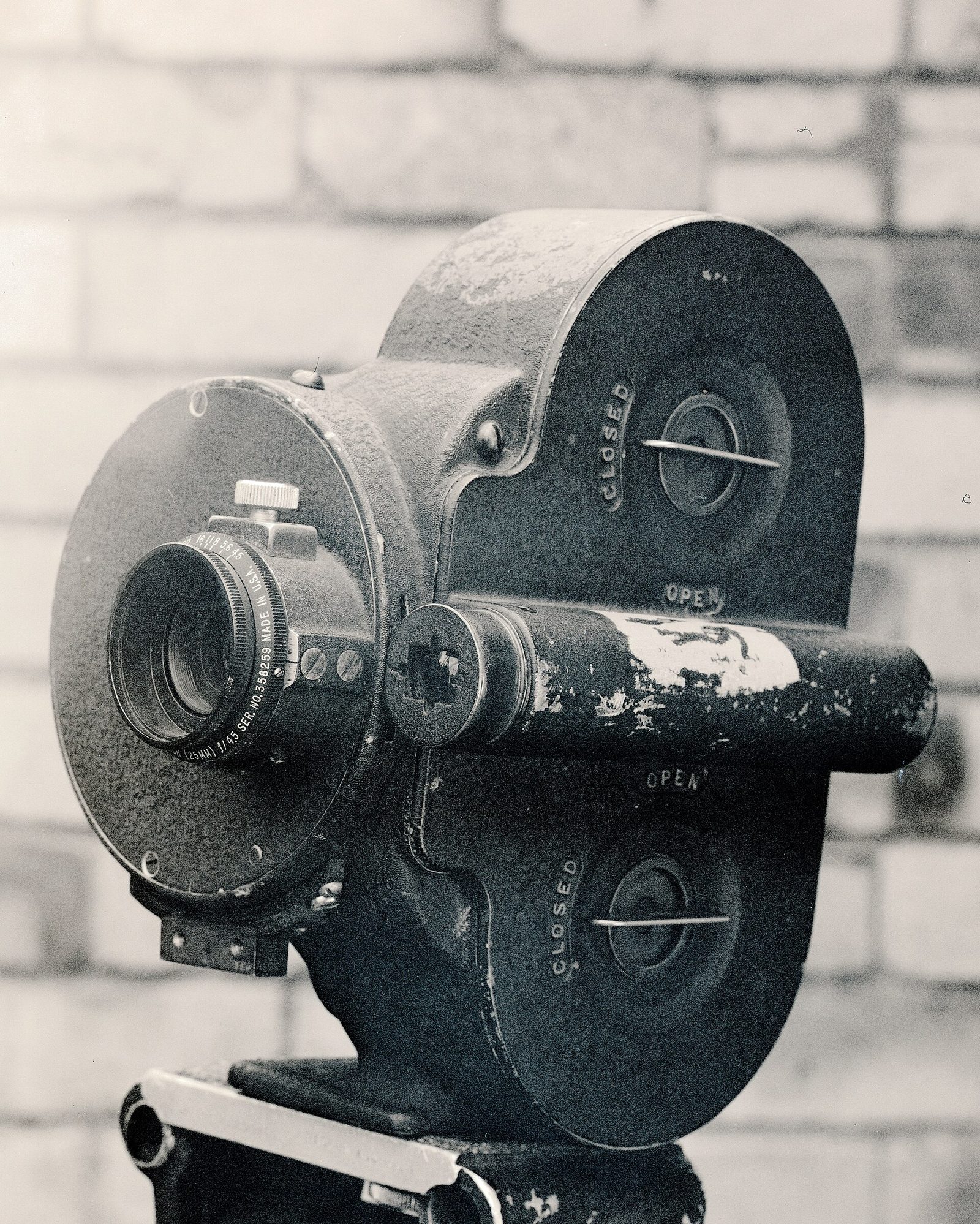 A worn single-lens Bell & Howell Eyemo on a tripod head, its paint chipped, with OPEN and CLOSED markings cast into the body.
