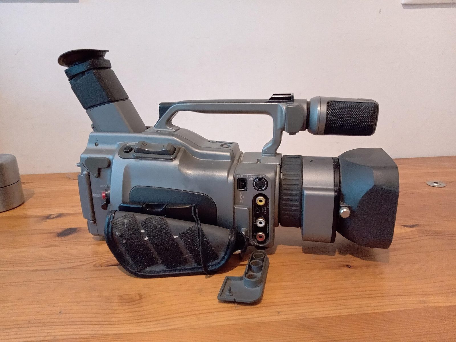 The opposite side of a Sony DCR-VX1000 showing its FireWire, S-Video and composite connection ports and a hand strap.